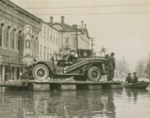 Flood on Market street. Includes the Odd Fellow building in the background. A fire engine on a boat surrounded by water and other men in boats. 